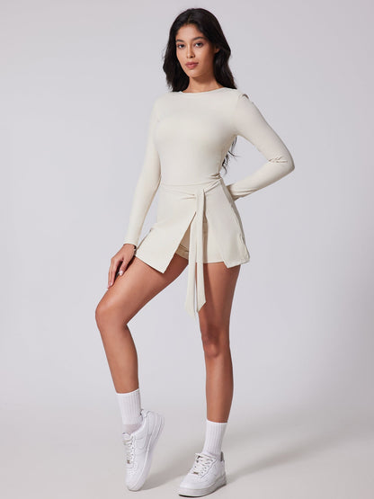 Woman wearing a white long-sleeve top and skirt with white sneakers on a light gray background