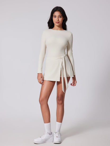 Woman wearing a white long-sleeve dress with a tie detail on a plain background