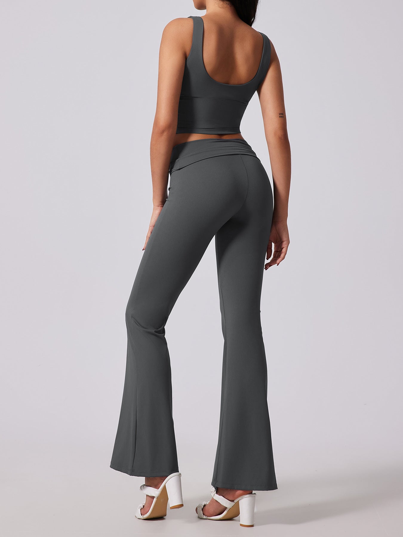 Person wearing a dark gray athletic outfit with flared pants on a light gray background