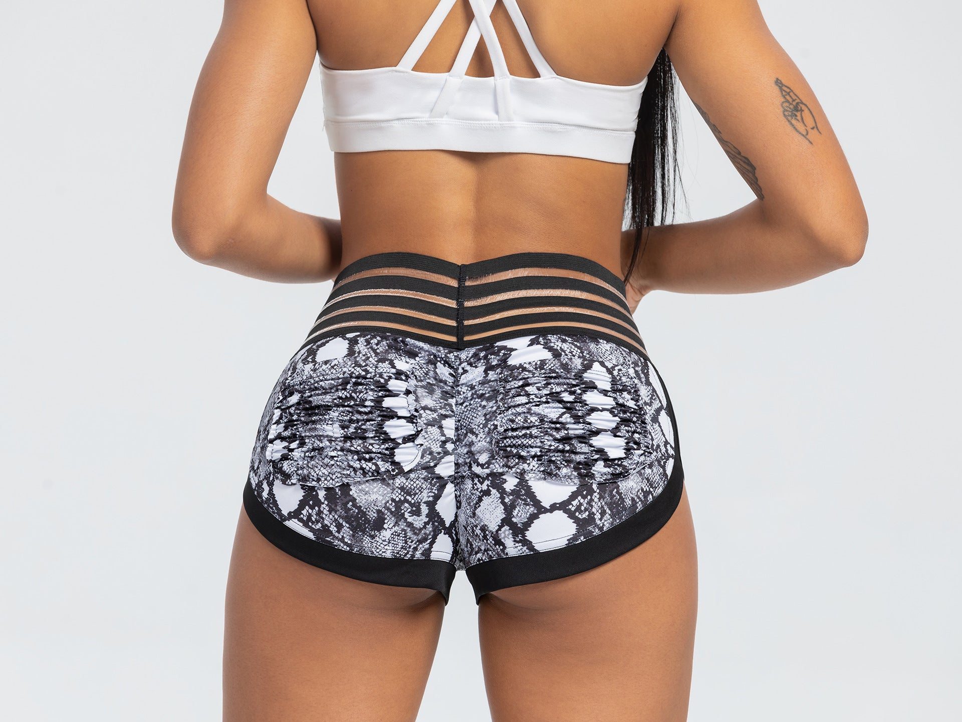 Person wearing a white sports bra and black and white patterned shorts on a light gray background