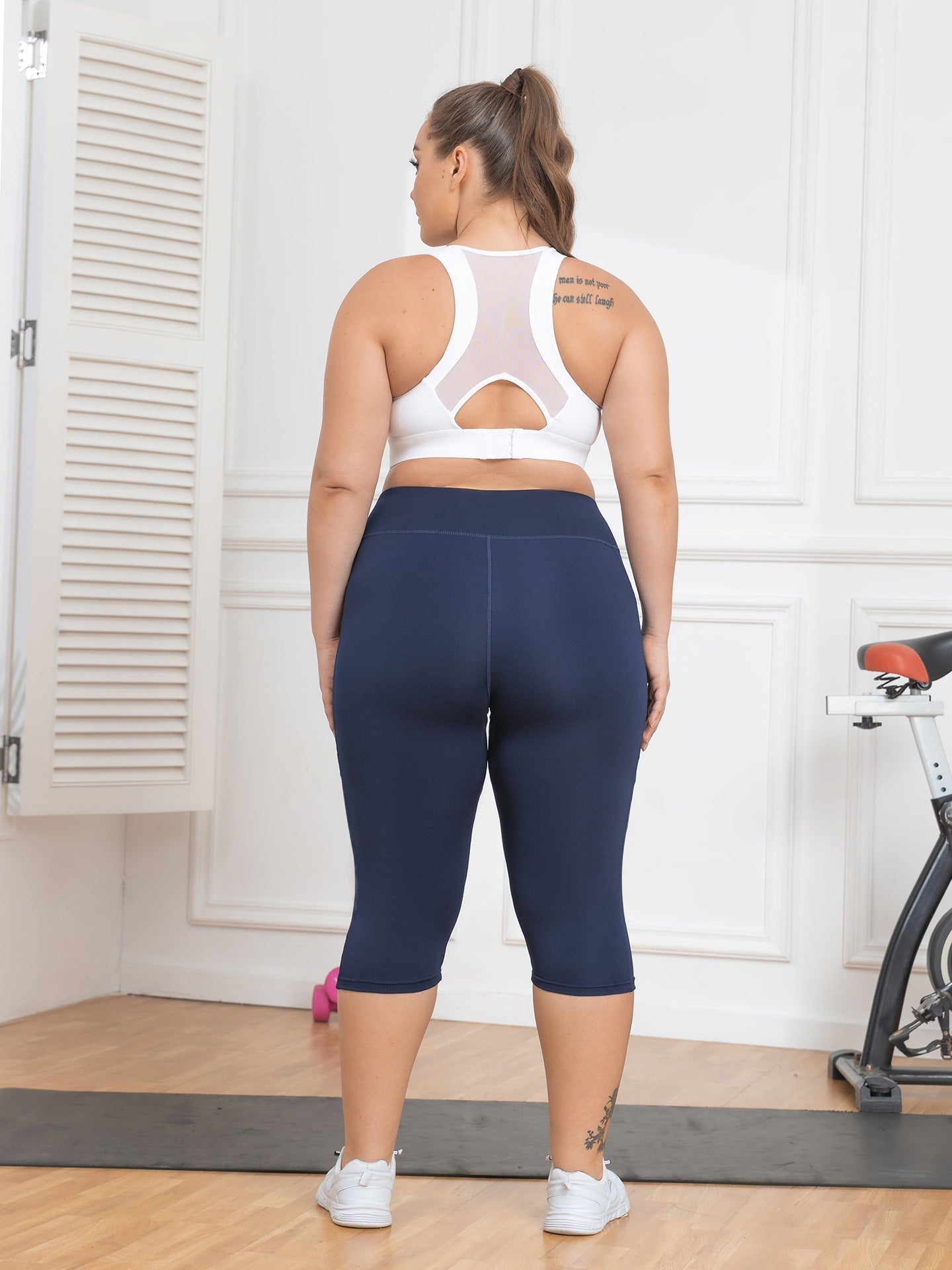 Person wearing navy blue leggings and a white sports bra in a home setting.