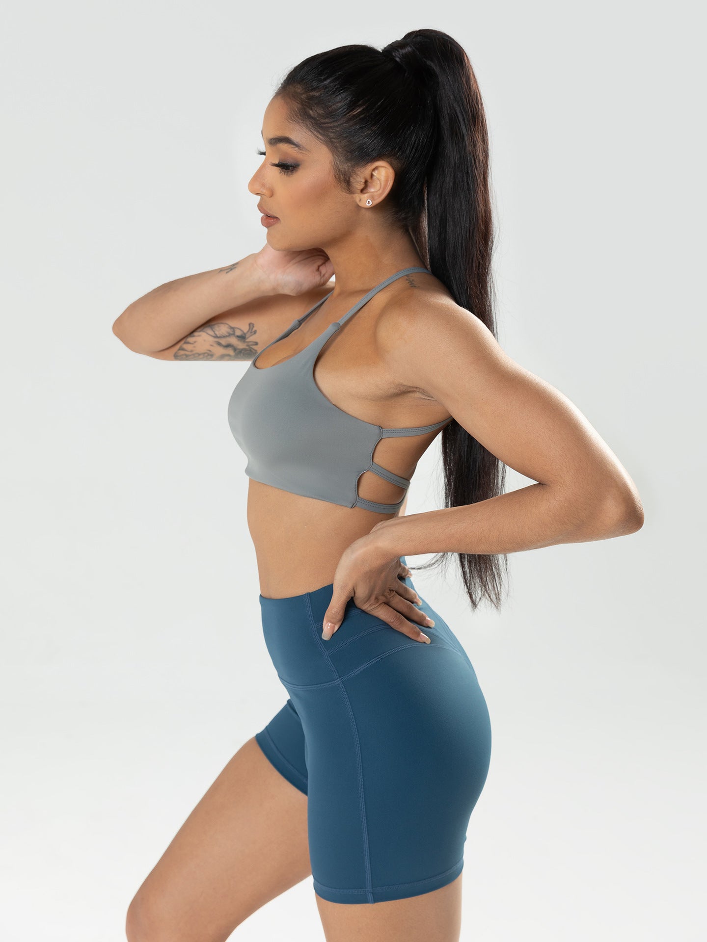 Woman wearing a gray sports bra and blue shorts on a white background
