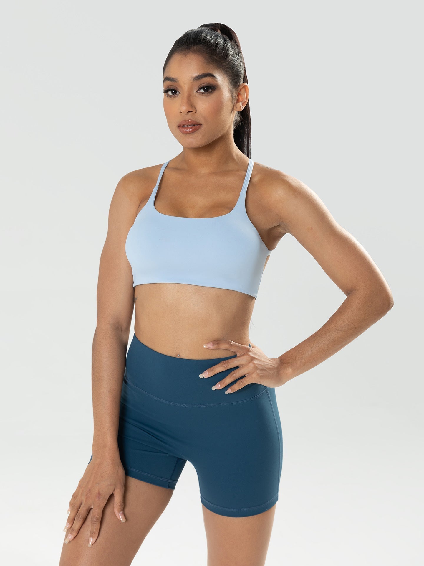 Woman wearing a light blue sports bra and dark blue shorts on a white background