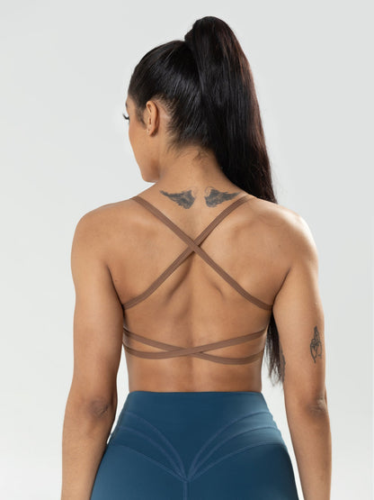 Woman wearing a strappy top and blue leggings against a plain background