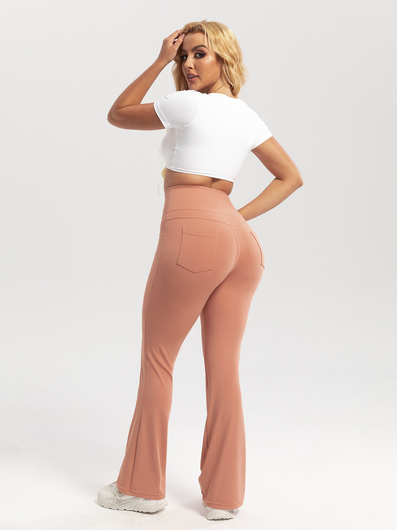Woman wearing a white crop top and tan flared pants on a white background