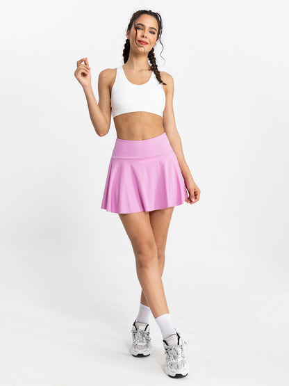 Woman wearing a white sports bra and pink tennis skirt on a white background