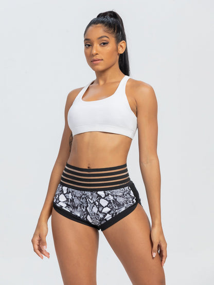 Woman wearing a white sports bra and black and white patterned shorts on a light gray background