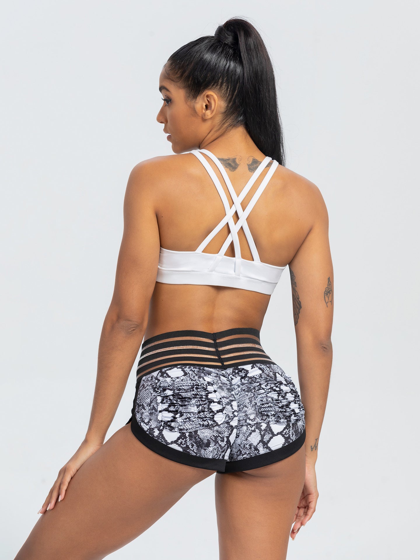 Woman wearing a white sports bra and black patterned shorts on a light gray background