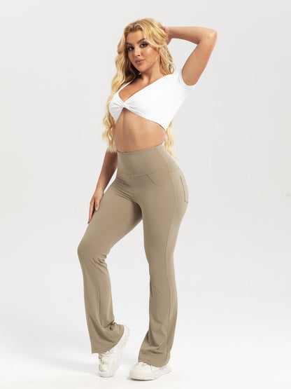 Woman wearing beige pants and a white top on a plain background